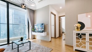 Una sala de estar moderna con un ventanal grande, un televisor de pantalla plana, una mesa de centro de vidrio y un mueble blanco con objetos decorativos.
