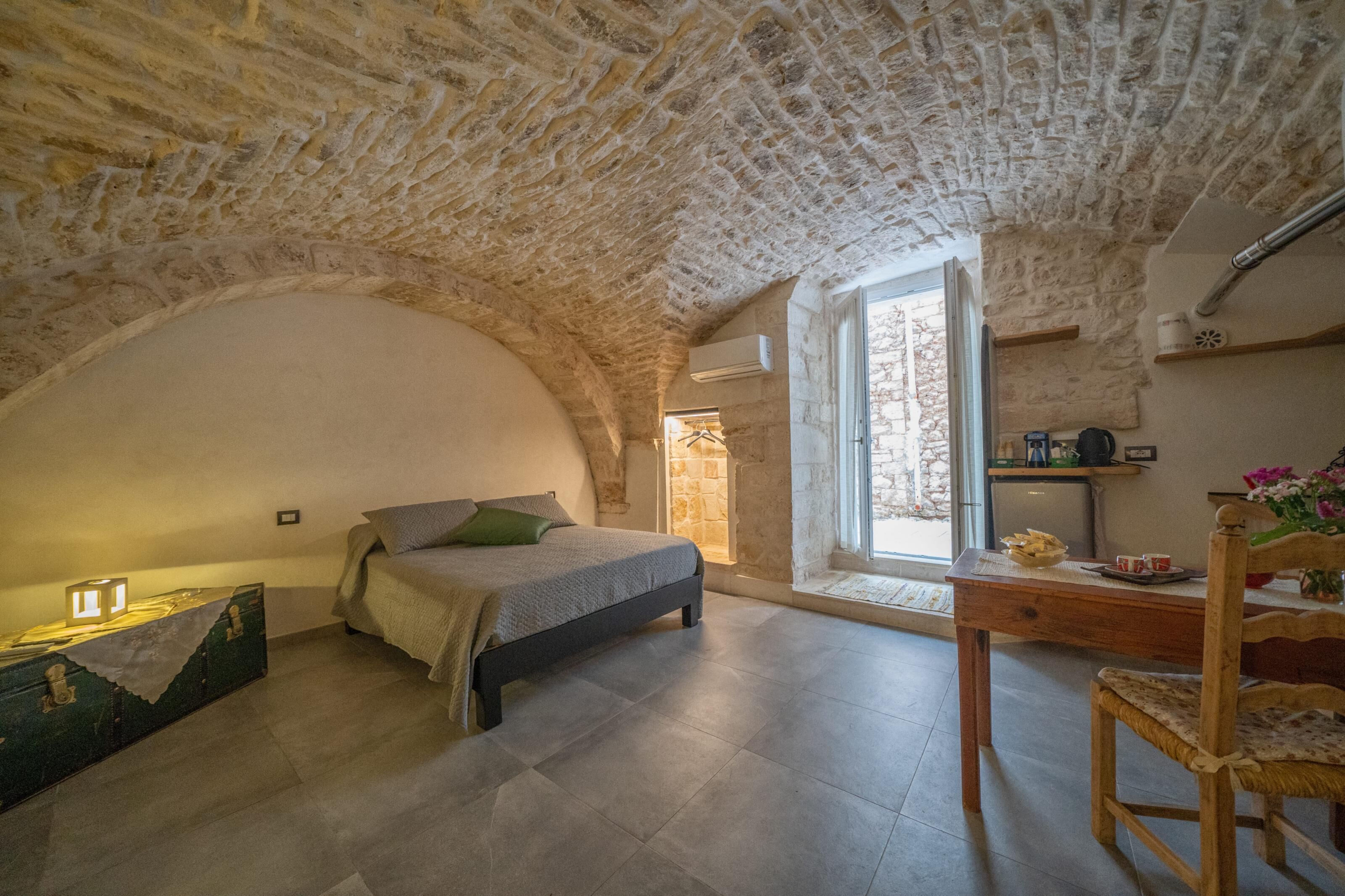 A bedroom with a stone ceiling, a bed, a desk, and a window.
