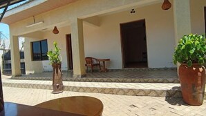 An outdoor seating area with a tiled floor, potted plants, and a wooden chair. - The Marais Hotel and Suites- SIAYA (Siaya)
