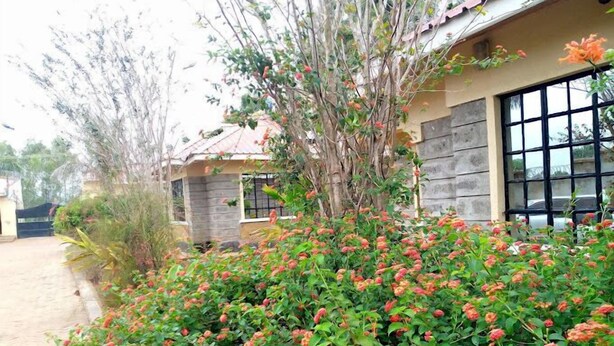 A house with a stone facade, a large window, and a garden with flowering plants. - The Marais Hotel and Suites- SIAYA (Siaya)