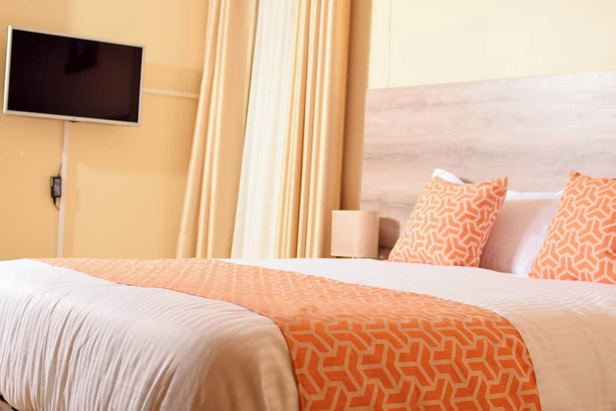 Una habitación de hotel con una cama, un televisor fijado a la pared y una ventana con cortinas.