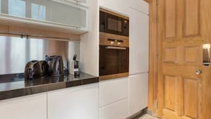 Una cucina moderna con mobili bianchi, una porta in legno e un piano di lavoro con bollitore e macchina da caffè.
