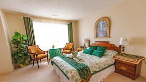 A bedroom with a large bed, two chairs, a nightstand, a lamp, a mirror, and a potted plant. - Cozy tidy private | Sunset Garden (Cochrane)