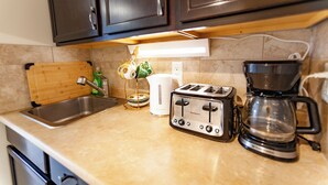 A kitchen with a sink, toaster, coffee maker, and a wooden cutting board. - Cozy tidy private | Sunset Garden (Cochrane)