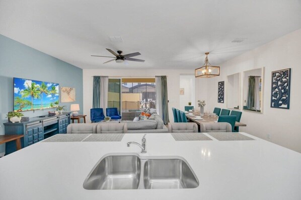 A modern living room with a central island, a dining area, and a kitchen with a large sink.