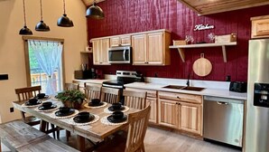 A kitchen with wooden cabinets, a stainless steel refrigerator, and a dining table set for four. - Bearly Dreaming Elite Location Hot Tub & Game Room (Gatlinburg)