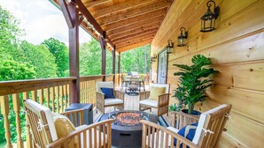 A wooden deck with outdoor furniture, a fire pit, and a view of the forest. - Bearly Dreaming Elite Location Hot Tub & Game Room (Gatlinburg)