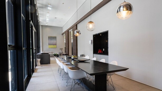 Un comedor moderno con una mesa larga, sillas blancas e iluminación colgante.