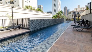 Una piscina en la azotea con terraza de madera, sillas de descanso y un borde de azulejos.