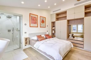 Un dormitorio moderno con ducha de vidrio, una cama con ropa de cama blanca y un armario con estantes abiertos.