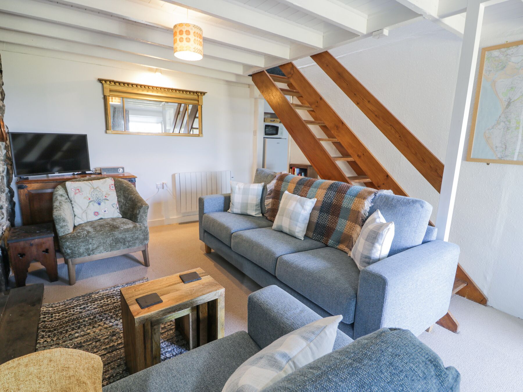 A living room with a sofa, armchairs, a coffee table, a TV, and a staircase.