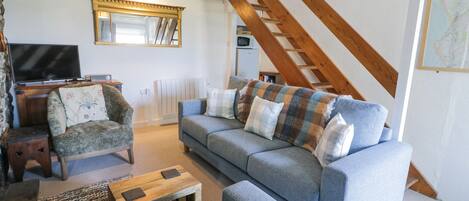 A living room with a sofa, armchairs, a coffee table, a TV, and a staircase.