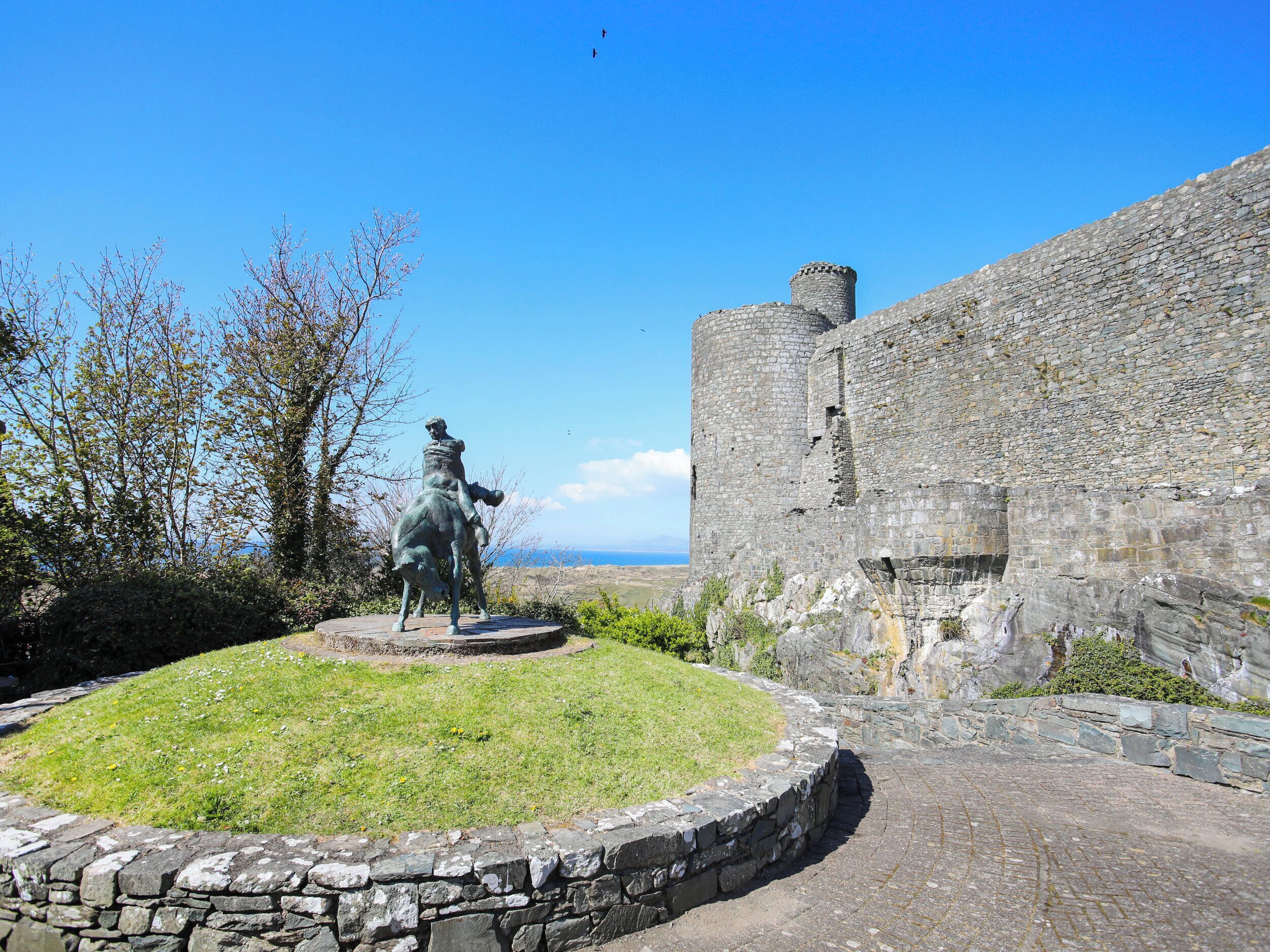 A statue of a man on horseback in front of a stone wall with a clear sky in the background.