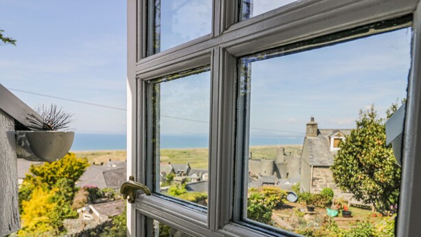 A window with a view of a rural landscape, including stone buildings and greenery. - Pen Y Bryn Bach (Harlech)