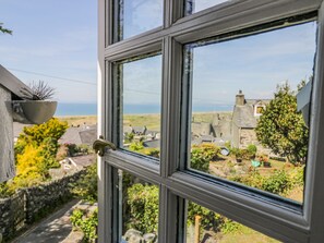 A window with a view of a rural landscape, including stone buildings and greenery.