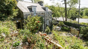 A stone house with a sloped roof, surrounded by lush greenery and trees. - Pen Y Bryn Bach (Harlech)