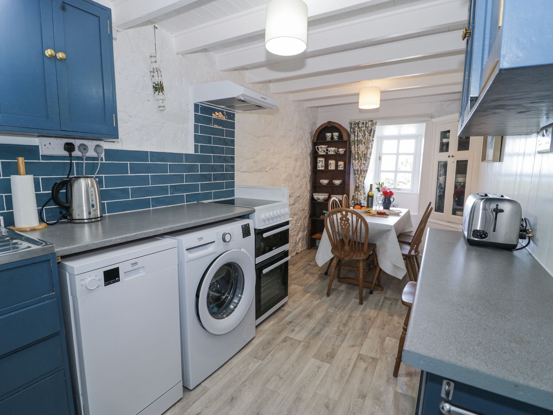 Une cuisine compacte équipée d’un lave-linge, d’une bouilloire, d’un grille-pain et d’un coin repas avec une table et des chaises.