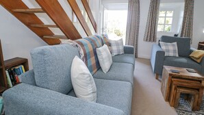 A spacious living room with a large blue sofa, a wooden coffee table, and a bookshelf filled with books. - Pen Y Bryn Bach (Harlech)