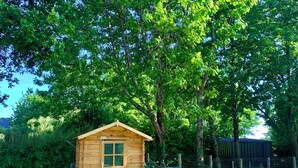 A small wooden cabin with a gabled roof, surrounded by lush greenery and trees.