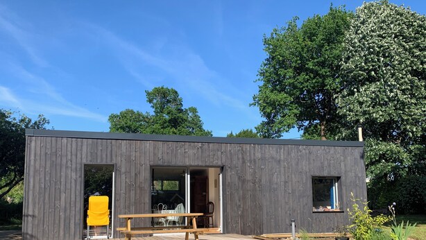 A modern wooden building with a deck, a bench, and a yellow planter.