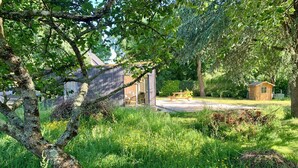 A lush garden with a picnic table, a wooden shed, and a house with a sloped roof.