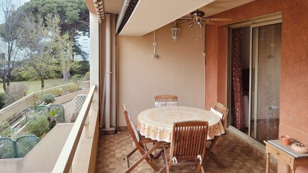 A balcony with a round table and chairs, a ceiling fan, and a view of trees and buildings. - Apartment in the port of Hyères (Hyères)