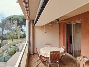 A balcony with a round table and chairs, a ceiling fan, and a view of trees and buildings. - Apartment in the port of Hyères (Hyères)