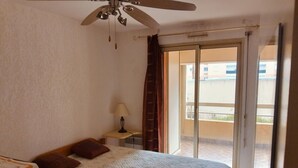 A bedroom with a bed, a nightstand, a lamp, a ceiling fan, and a sliding glass door leading to an outdoor balcony. - Apartment in the port of Hyères (Hyères)