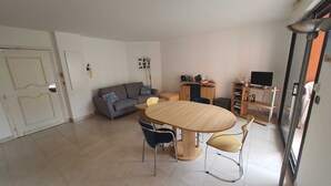 Una sala de estar moderna con un sofá gris, una mesa de comedor de madera y un mueble para televisión con un televisor de pantalla plana.