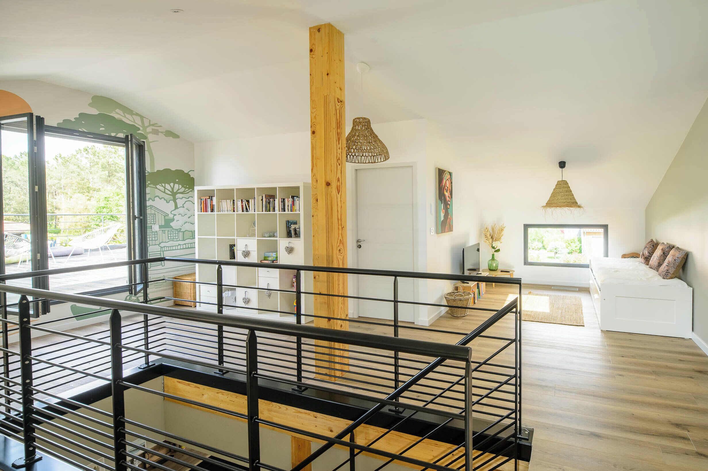 Een ruime loft met een houten trap, een entresol en een groot raam met uitzicht op groen.
