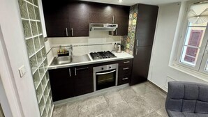 A compact kitchen with dark cabinets, a gas stove, a sink, and a window with blinds.