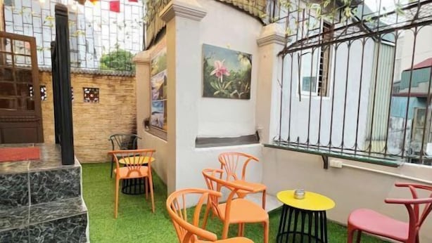 An outdoor seating area with green artificial grass, orange and pink chairs, and yellow tables. - Heritage Corner Hostel (Hanoi)