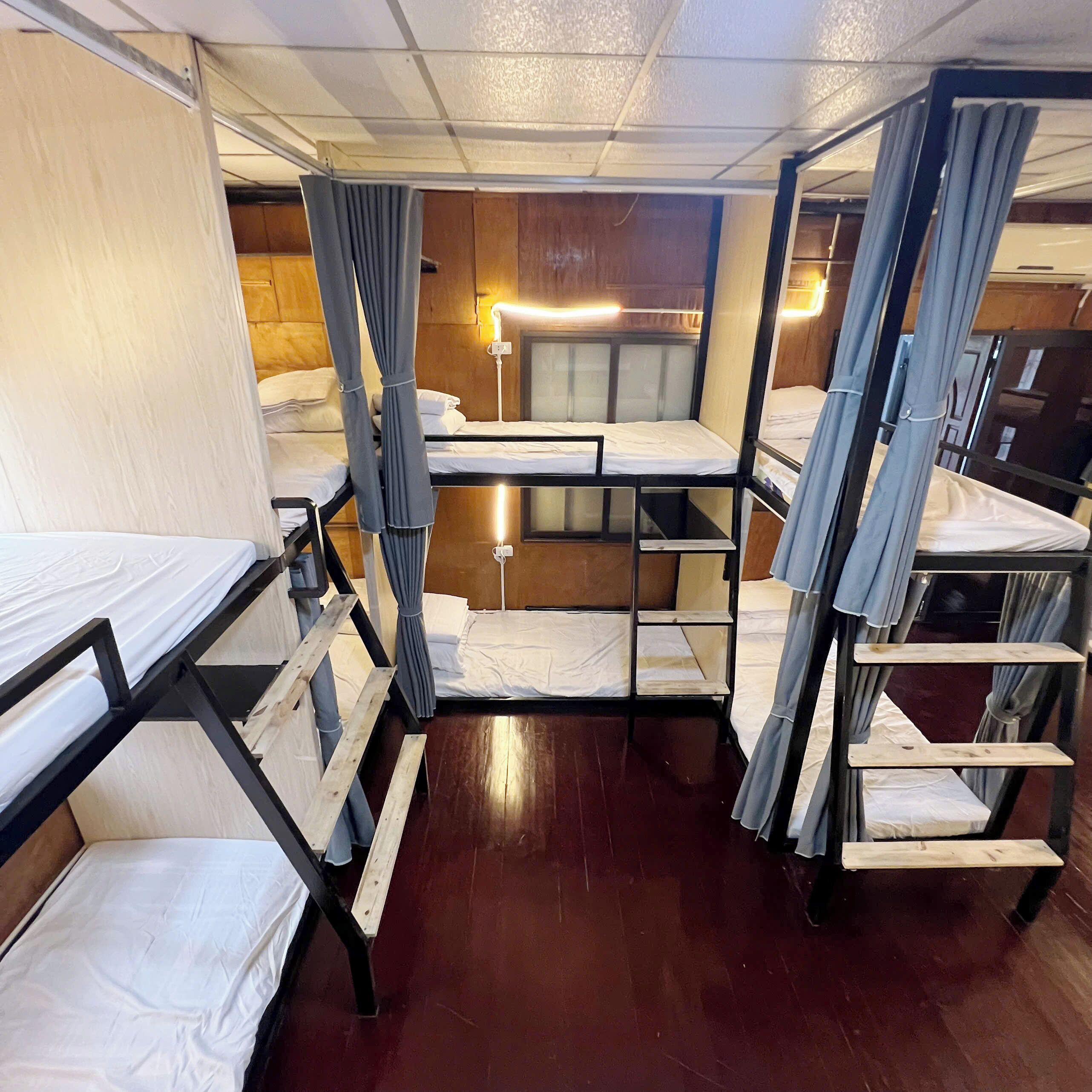 Ein kleines Hotelzimmer mit Etagenbetten, Holzboden und einer Nachttischlampe.