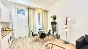 A compact living space with a kitchenette, a dining area with a round table and chairs, a sofa, and a floor lamp.