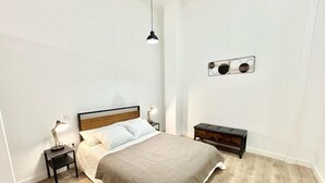 A bedroom with a bed, bedside tables, a hanging light, and a wall-mounted decoration.