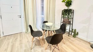 A dining area with a round glass table, four black chairs, a white bowl, a plant on a shelf, and a cactus on the floor.