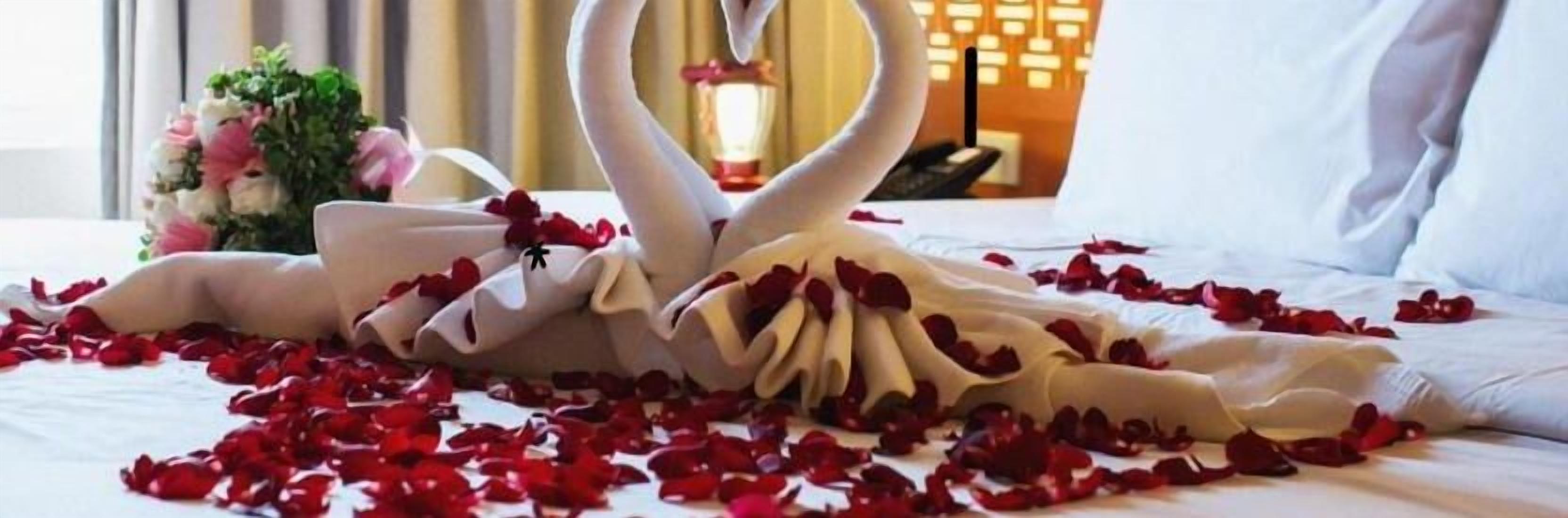 A bed with rose petals and a swan-shaped pillow.