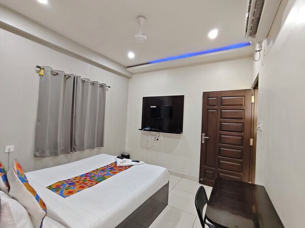 A bedroom with a bed, a TV mounted on the wall, a wooden door, and a ceiling fan. - Hotel Grandview And coliving (Hyderabad)