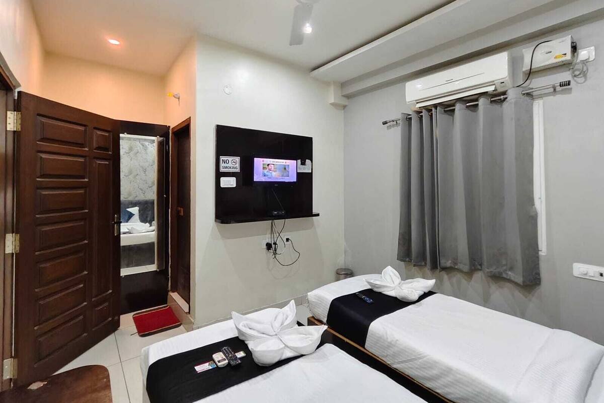 Een hotelkamer met twee bedden, een aan de muur bevestigde televisie, een airconditioning en een plafondventilator.