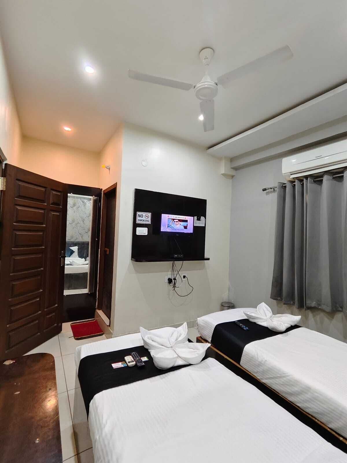 A hotel room with two beds, a TV mounted on the wall, a ceiling fan, and a door leading to a bathroom.