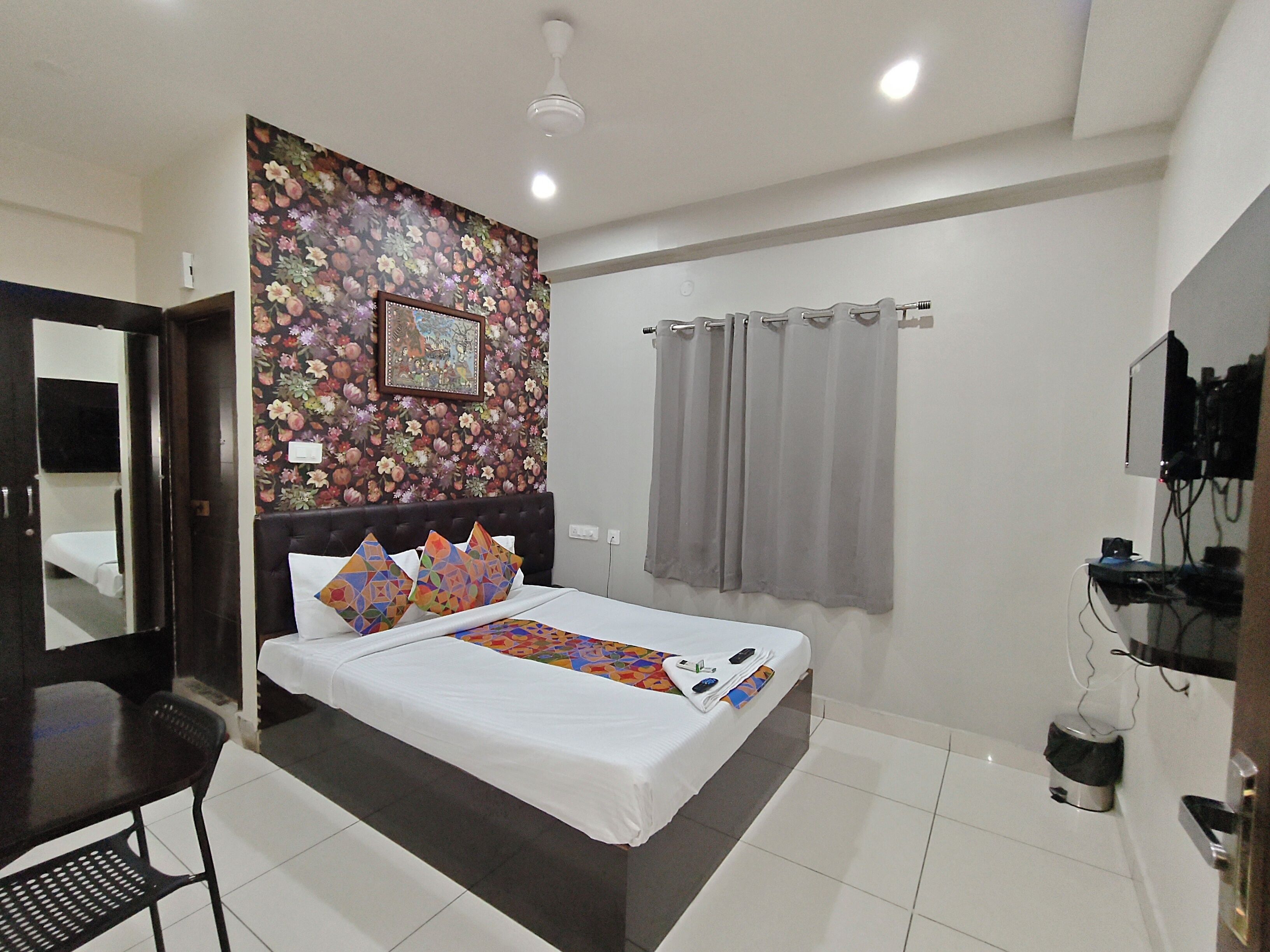 Habitación de hotel con cama, escritorio, silla, televisor y zona de ducha.
