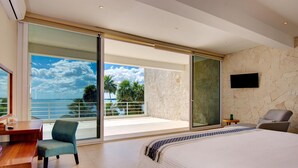 Un dormitorio con una cama grande, un escritorio, una silla y vistas al océano a través de una puerta corrediza de vidrio.
