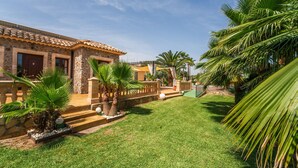A stone building with a tiled roof, a well-maintained lawn, and palm trees.