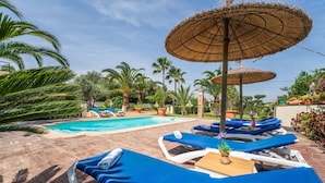 A pool area with lounge chairs and umbrellas, surrounded by palm trees and potted plants.