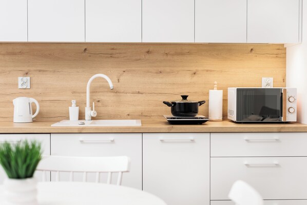 Une cuisine moderne avec des meubles blancs, un plan de travail en bois, un évier, une bouilloire, un four à micro-ondes et une casserole noire.