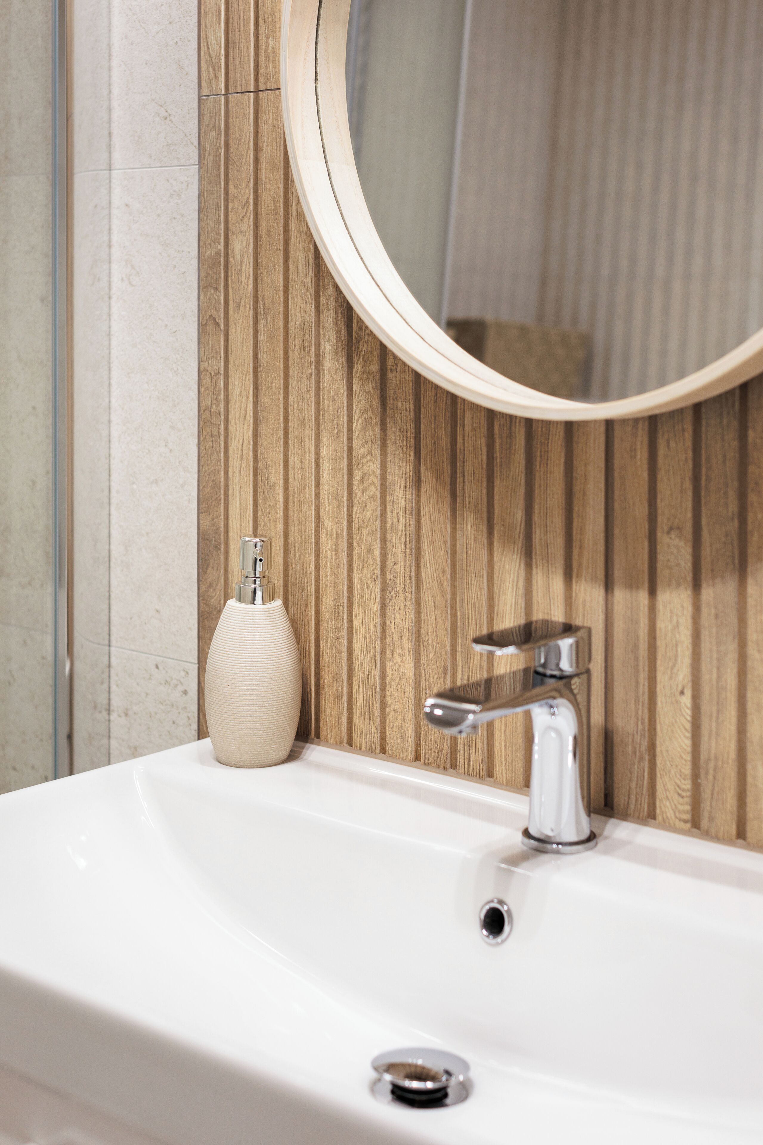 Un baño con lavamanos blanco, un grifo moderno y pared de paneles de madera.
