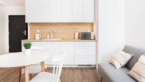 A compact kitchen with white cabinets, a wooden countertop, a sink, a microwave, and a small potted plant. - City of the Kings-Riverside WT2 (Kraków)
