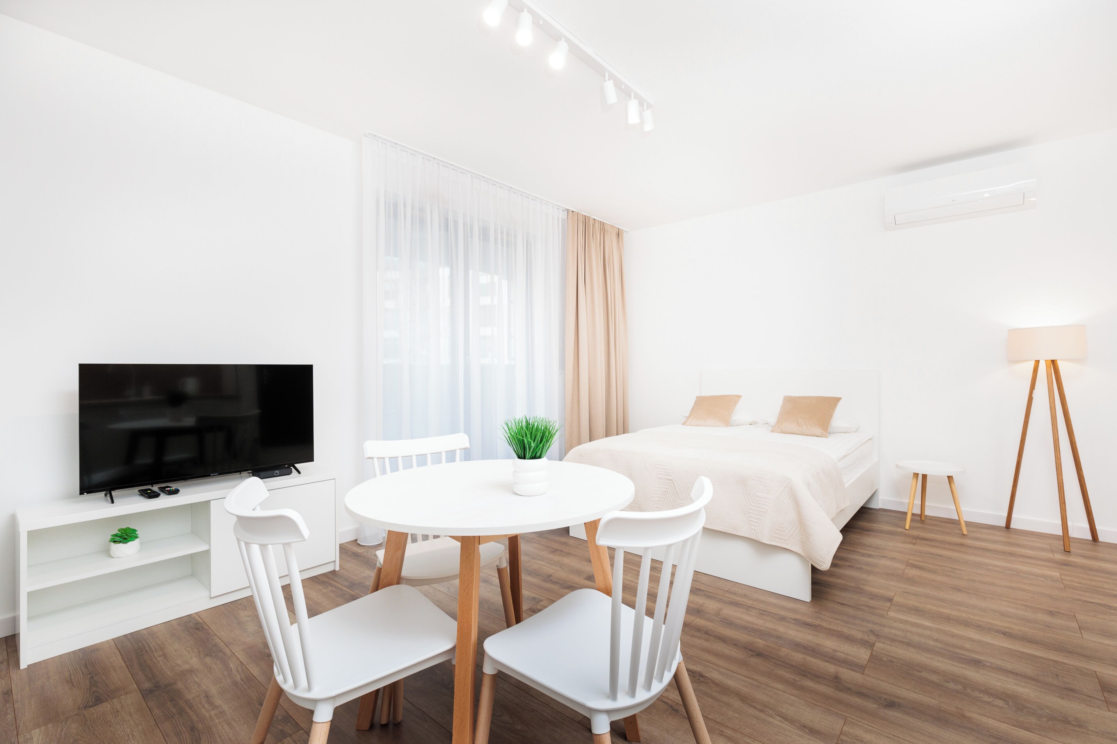 Una habitación de hotel moderna con televisión de pantalla plana, una mesa redonda con sillas, una cama con edredón blanco y una lámpara de noche.