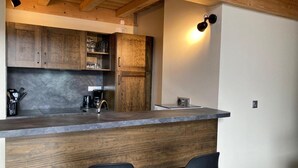 A modern kitchen with wooden cabinets, a dark countertop, and two black bar stools. - 250m from ski slopes, 6th floor, balcony, tv, 99m², Les 2 Alpes (Les Deux Alpes)