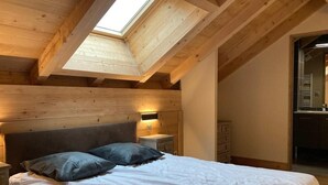 A bedroom with a sloped ceiling, wooden beams, a skylight, a bed with white bedding, two pillows, a nightstand, and a dresser. - 250m from ski slopes, 6th floor, balcony, tv, 99m², Les 2 Alpes (Les Deux Alpes)